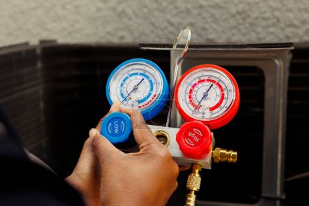 Pressure meters able to detect damaged expansion valve and excessive freon in condenser, close up. Knowledgeable professional using manifold indicator to read refrigerant levels in outside hvac system