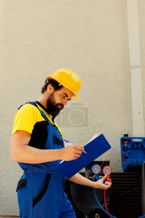 Photo for Competent mechanic filling out revision of insurance contract for home owner to sign after finishing repairments on air conditioner. Expert repairman writing down cost of fixed internal components - Royalty Free Image