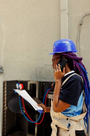 Téléchargez les photos : Spécialiste afro-américain demandant conseil au gestionnaire au téléphone sur le climatiseur a besoin d'être entretenu. Apprenti vérifiant le plan d'entretien après avoir terminé le nettoyage des pièces internes - en image libre de droit