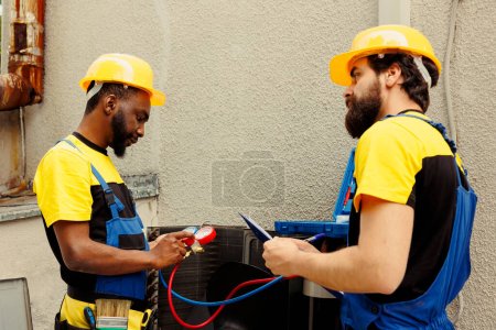Photo for Efficient technicians commissioned to do condenser check, refilling freon. Seasoned mechanics using professional manifold gauges to precisely measure the pressure in outside air conditioner - Royalty Free Image