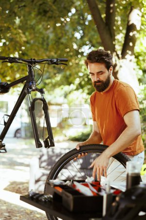 Photo for In home yard, young energetic man is using expert tools to replace damaged bike wheel. Servicing on disassembled bicycle outside for pleasure cycling is a committed, healthy caucasian male cyclist. - Royalty Free Image