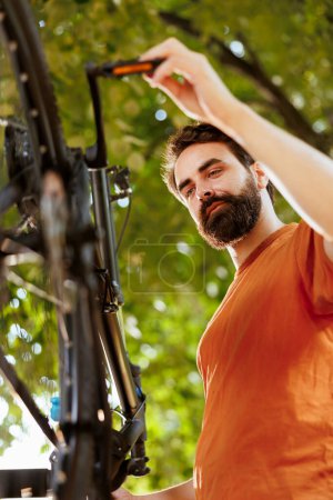 Photo for Committed energetic man fine-tunes and adjusting bike pedals in home yard. Closeup shot of athletic caucasian male meticulously examining and correcting damages on bicycle crank arm. - Royalty Free Image