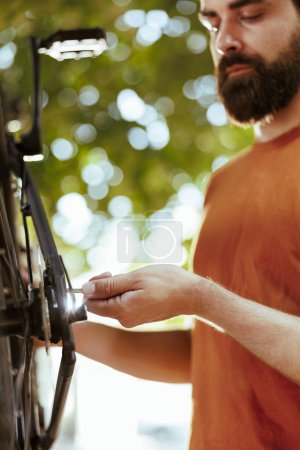 Photo for Close-up shot of committed caucasian man gripping spanner for tightening bicycle parts outdoor. Detailed image of male cyclist repairing bike wheel for secure leisure cycling. - Royalty Free Image