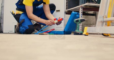 Photo for Ground level shot of capable specialist assembling manifold meters before mounting it on condenser. Seasoned mechanic looking for freon leaks leading to weaker cooling efficiency - Royalty Free Image
