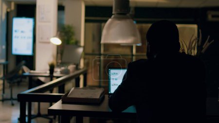 Photo for Employee left alone in the dark overnight in office, solving project tasks before next day deadline. Accountant working by himself in workspace, trying to keep up with paperwork - Royalty Free Image