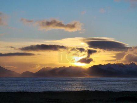 Téléchargez les photos : Heure d'or islandaise sur le front de mer avec plage de sable noir gelé et montagnes rocheuses, coucher de soleil spectaculaire lueur. Paysage majestueux de lumière du soleil près du rivage de l'océan, paradis froid. - en image libre de droit
