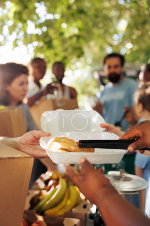 Photo for Photo focus on african american volunteer serving warm meal to needy hungry caucasian individual at a food drive. Detailed shot of poor less privileged person receiving free food from charity worker. - Royalty Free Image
