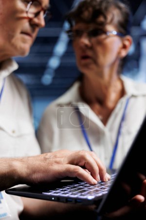 Photo for Octogenarian IT developers running analysis on server rows helping businesses manage databases, host websites and store files. Licensed programmers auditing high tech data center gadgets - Royalty Free Image