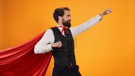 Téléchargez les photos : Puissant majordome héros posant avec cape rouge sur fond jaune, dédié à servir les consommateurs dans un restaurant gastronomique. Concept de personnage de super-héros confiant, traiteur de luxe. - en image libre de droit