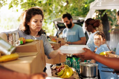 Foto de Diverso grupo proporciona ayuda, repartiendo comidas a personas pobres y necesitadas. Voluntarios de todos los orígenes se reúnen para ayudar a las personas sin hogar, ofreciendo apoyo a través de una campaña de caridad de alimentos. - Imagen libre de derechos