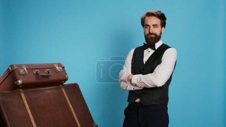 Photo for Hotel porter with baggage in studio, providing outstanding service to carry luggage for guests. Professional bellhop or doorman with suit and tie feeling confident and determined on camera. - Royalty Free Image