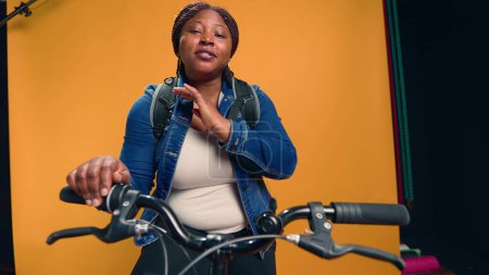 Téléchargez les photos : Vidéo montrant un messager afro-américain à vélo expliquant avec plaisir son travail de service de messagerie. Jeune femme noire à vélo parlant à la caméra du service de livraison de nourriture. Coup de main. - en image libre de droit