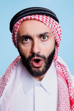 Photo for Muslim man with open mouth wearing traditional checkered ghutra headscarf studio closeup portrait. Arab person in islamic headdress showing emotion on face and looking at camera - Royalty Free Image