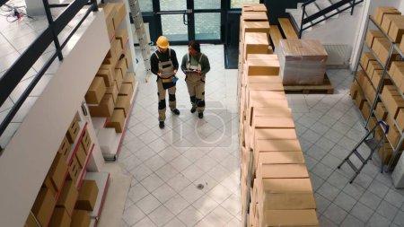 Photo for Aerial drone shot of warehouse employees starting shift, inspecting cardboard box parcels before clearing them for shipping. Repository executives making sure stocks and inventory are well organized - Royalty Free Image