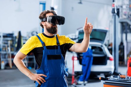 Photo for Focused technician in car service uses virtual reality to visualize automobile components in order to repair them. Garage expert wearing high tech vr headset while fixing vehicle issues - Royalty Free Image