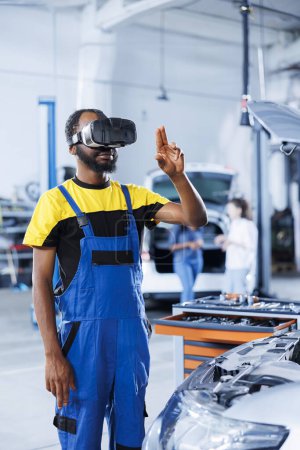 Photo for Professional in auto repair shop using virtual reality technology to visualize car alternator in order to fix it. Effective garage employee wearing futuristic vr headset while mending faulty vehicle - Royalty Free Image