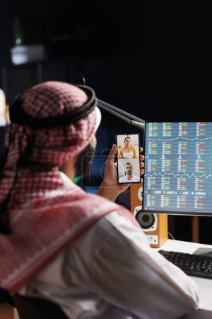 Foto de Hombre de Oriente Medio absorto en una videollamada con un compañero de trabajo en su teléfono celular. Hombre musulmán utiliza la tecnología inalámbrica para el trabajo y la investigación, mostrando sus habilidades de comunicación digital. - Imagen libre de derechos
