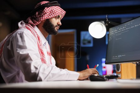 Téléchargez les photos : L'homme musulman tape le code sur un PC de bureau. Il excelle dans la programmation d'applications et met en valeur son expertise dans le développement logiciel et les algorithmes. Cette image représente l'évolution du monde de la technologie numérique. - en image libre de droit