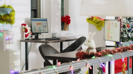 Foto de Árbol de pino de Navidad adornan con bolas y luces de Navidad en la oficina vacía. Estadísticas de auditoría empresarial en pantallas de ordenador en Navidad adornan el lugar de trabajo sin trabajadores durante la temporada de vacaciones de invierno - Imagen libre de derechos