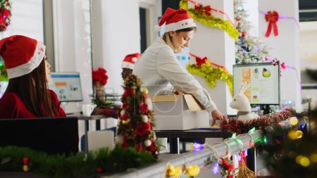 Foto de Pissed employee packs desk belongings and steals Christmas office ornaments on last day at work to feel better. Vengeful woman getting fired from job during layoffs, delighted about retribution - Imagen libre de derechos