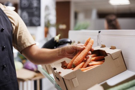 Photo for Trader fills up crates on low carbon footprint zero waste shop shelves with locally grown vegetables. Storekeeper restocks local groceries store with food items, close up shot on carrots - Royalty Free Image