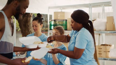 Foto de Las mujeres voluntarias de diferentes etnias proporcionan a las personas sin hogar fruta fresca y comidas gratis. Voluntariado en la campaña de comida, damas caucásicas y afroamericanas ayudan a los necesitados y menos afortunados. - Imagen libre de derechos