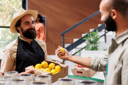Photo for Smiling customer admiring fresh lemon picked from the box held by caucasian vendor. Friendly storekeeper presenting locally grown organic produce to middle eastern man. - Royalty Free Image