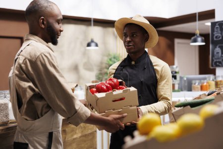 Téléchargez les photos : Un Afro-Américain vend des produits frais et biologiques dans un supermarché respectueux de l'environnement, offrant une variété de fruits et légumes durables pour des clients soucieux de leur santé. - en image libre de droit