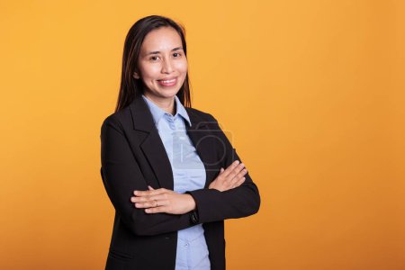 Photo for Successful joyful woman standing in arm crossed posing over yellow background, smiling at camera during studio shoot. Smiling asian model with cheerful expression enjoying break time - Royalty Free Image