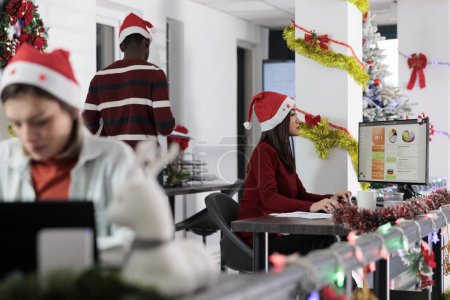 Photo for Focused employees researching key data for company project during Christmas holiday season. Multiethnical business team solving tasks in festive decorated office before approaching deadline - Royalty Free Image