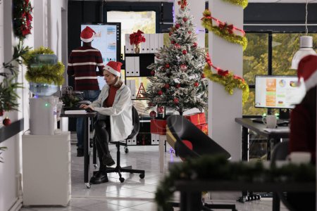 Photo for Business team working in busy festive decorated office during Christmas holiday season. Hardworking employees solving various company project tasks in xmas ornate workspace - Royalty Free Image