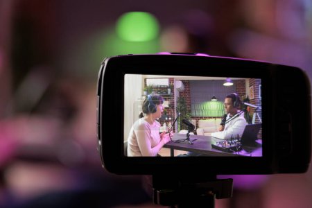 Photo for Close up shot focused on preview image on professional camera with podcast host and african american guest enjoying conversation in blurry background. Professional recording equipment in home studio - Royalty Free Image