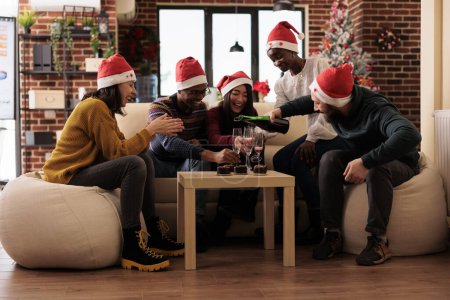 Téléchargez les photos : Des employés joyeux versant de l'alcool dans des verres pour célébrer la saison de Noël. Heureux collègues se réunissant pour le dîner de Noël dans un bureau décoré - en image libre de droit