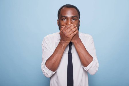 Photo for Terrified shocked black man keeps hands on his mouth and cannot believe something. Young individual feeling surprised after sharing a secret by mistake. Person mistakenly gossiped. - Royalty Free Image