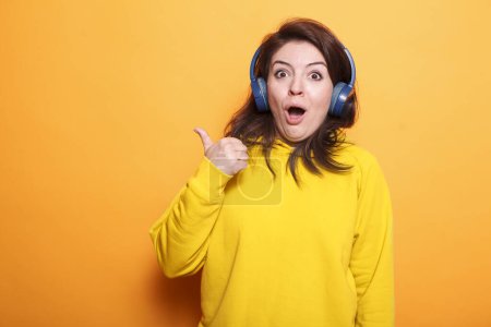 Photo for Confident, cheerful woman wearing headphones with a vibrant smile sings joyfully against isolated orange background. Her candid fashion and energetic hairstyle reflect her happy, expressive nature. - Royalty Free Image
