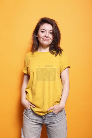 Photo for In studio, excited female person stands in front of isolated orange background. Joyful woman poses confidently, casually looking at the camera. Stylish adult with hands in pockets and a smile. - Royalty Free Image