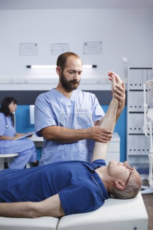 Téléchargez les photos : Patients âgés de sexe masculin recevant des soins ostéopathiques d'un médecin pour des douleurs aux bras. Blanc retraité homme aidé par infirmière dans les gommages bleus par l'exercice de physiothérapie. - en image libre de droit