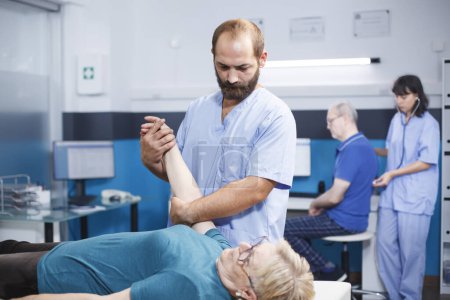 Photo for Elderly patient consults specialist assistant, receiving medical help for muscle pain. Nurse practitioner performs examination, stretches arms, and provides physiotherapy. - Royalty Free Image