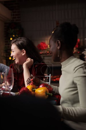 Photo for Cheerful woman having fun on xmas holiday, gathering with group of friends at dinner table and enjoying good food. Joyful festive person having fun with people at home, drinking wine. - Royalty Free Image
