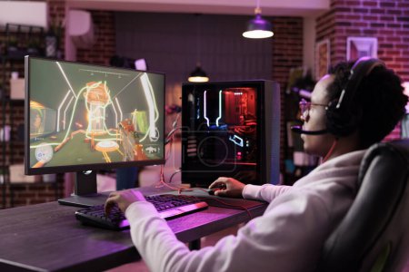Téléchargez les photos : Homme au mur de briques salon jouer à des jeux vidéo engageants sur PC de jeu au bureau de l'ordinateur, se refroidissant après le travail. Gamer luttant contre les ennemis dans le jeu de tir multijoueur en ligne - en image libre de droit