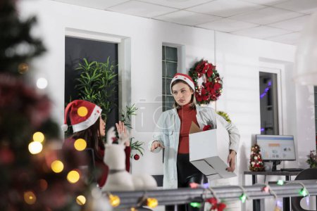 Photo for Excited company manager putting employees in Christmas spirit mood, bringing package at work full of festive ornaments. Management executive adorning workspace with xmas decorations - Royalty Free Image
