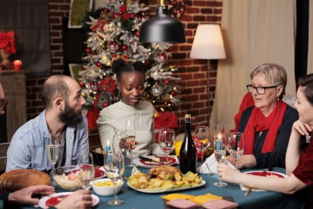 Téléchargez les photos : Les gens lever des verres pour porter un toast pendant le dîner de Noël, profiter du temps en famille à la maison avec de la nourriture traditionnelle. Divers amis faisant un discours pour remercier tout le monde pour célébrer autour de la table. - en image libre de droit