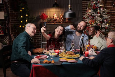 Téléchargez les photos : Famille prenant des photos lors du dîner de Noël avec une délicieuse nourriture et des verres de vin, faire des souvenirs pendant l'événement de vacances de décembre. Diverses personnes s'amusent avec des photos sur smartphone à la maison. - en image libre de droit