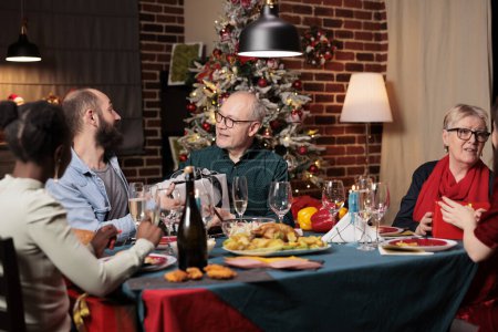 Téléchargez les photos : Père et fils échangeant des cadeaux lors du dîner de Noël, diverses personnes offrant des cadeaux pour répandre la positivité à la maison. Deux hommes se sentent joyeux avec des boîtes de goodies sur la célébration de Noël. - en image libre de droit