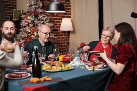 Photo for Diverse persons gathering around table to celebrate festive seasonal holiday, feeling cheerful during christmas eve dinner. Friends and family enjoying event at home with traditional homemade meal. - Royalty Free Image