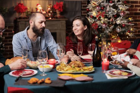Photo for Festive persons celebrating christmas event at table, gthering at home to enjoy traditional food. Diverse friends and family members having fun talking about memories, xmas celebration party. - Royalty Free Image
