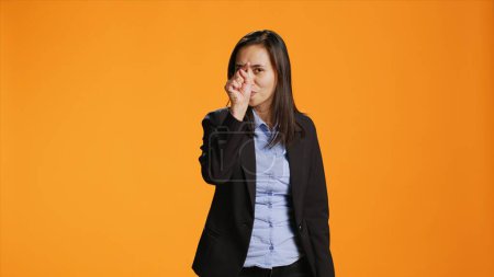 Foto de Empleado de la oficina asiática señalando con el dedo a la cámara, siendo serio y seguro sobre fondo naranja. La mujer vestida de formal indica algo delante de ella, apunta a la lente. - Imagen libre de derechos