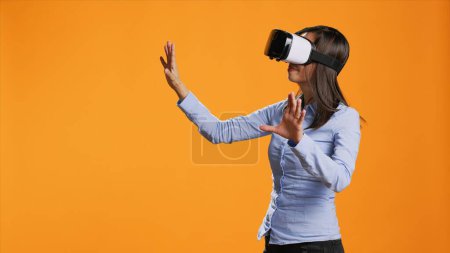 Foto de Mujer asiática opera auriculares de realidad virtual en la cámara, disfrutando de la inteligencia artificial metáfora en gafas modernas. Joven usando gafas vr para simulación de tecnología visual en estudio. - Imagen libre de derechos