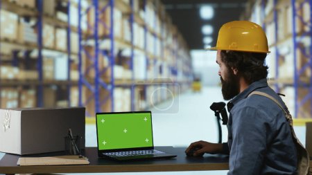 Photo for Customs compliance specialist uses greenscreen in depot warehouse, examining blank chromakey template. Male storage room administrator working with packages and copyspace display. - Royalty Free Image