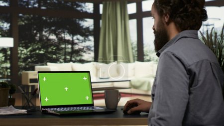 Photo for Young millionaire checks greenscreen template on laptop, getting cozy in his extravagant mountain resort. Wealthy businessman looks at blank mockup display on pc, teleworking. - Royalty Free Image